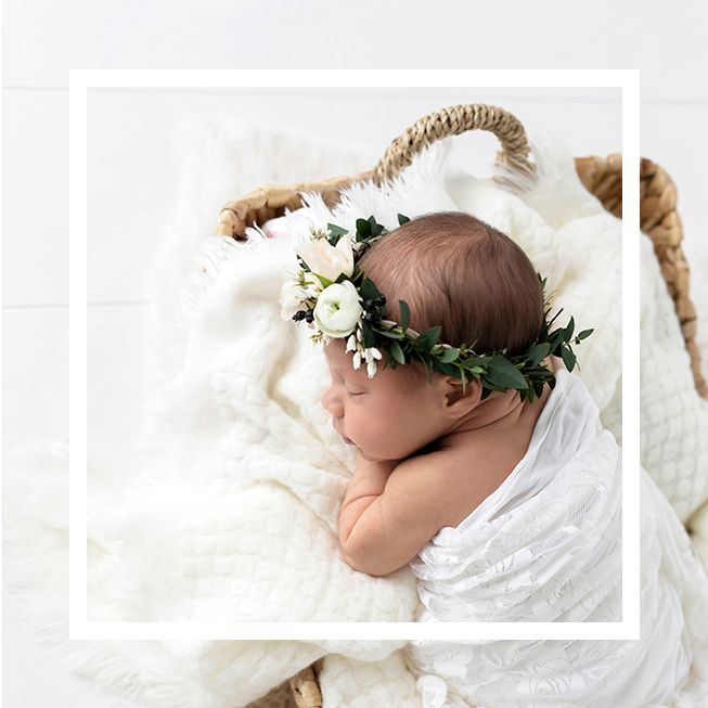 Professional newborn photographer in Menifee, CA: Sleeping newborn baby wearing a floral crown, nestled in a white blanket.