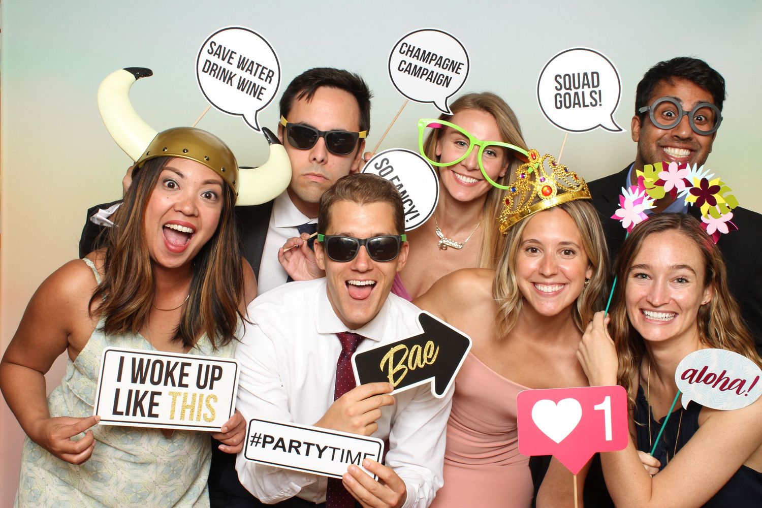 Group of friends posing with fun speech bubble props and accessories at a wedding photo booth.