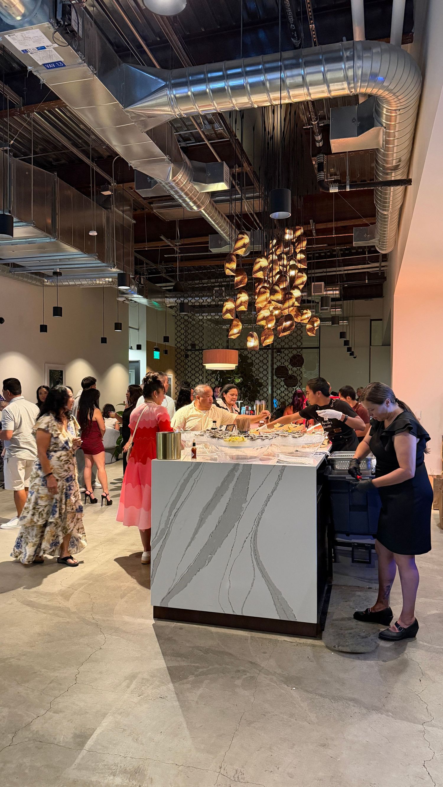 Guests mingle at a modern restaurant buffet with marble counter, decorative pendant lights, and exposed industrial ceiling. Walnut Creek.