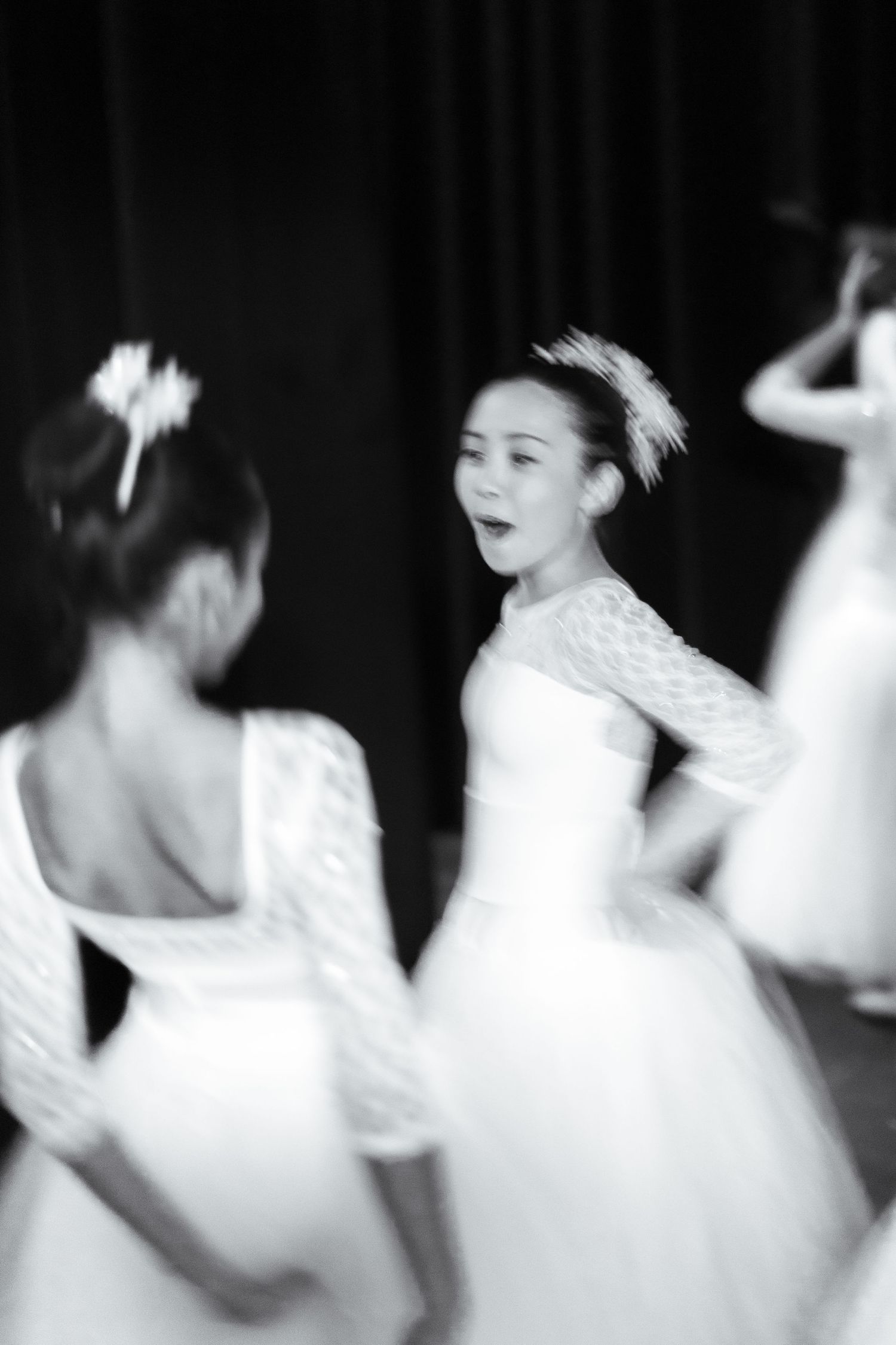 Young ballerinas in white lace dresses rehearse on stage in a blurred black and white dance recital photo. Las Positas College
