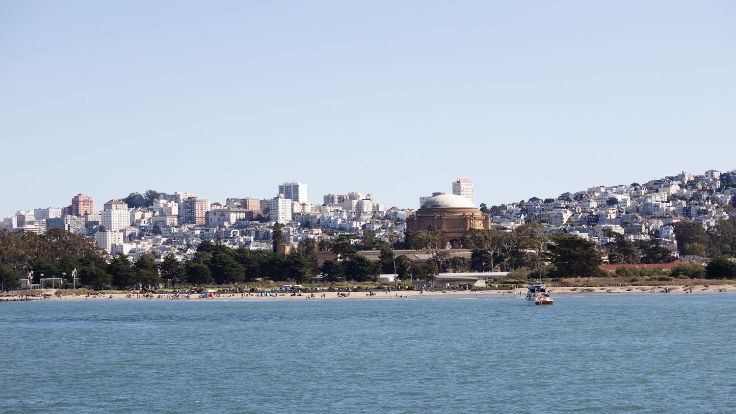 San Francisco skyline viewed from the bay with calm blue water, city buildings, and a domed structure under clear skies.