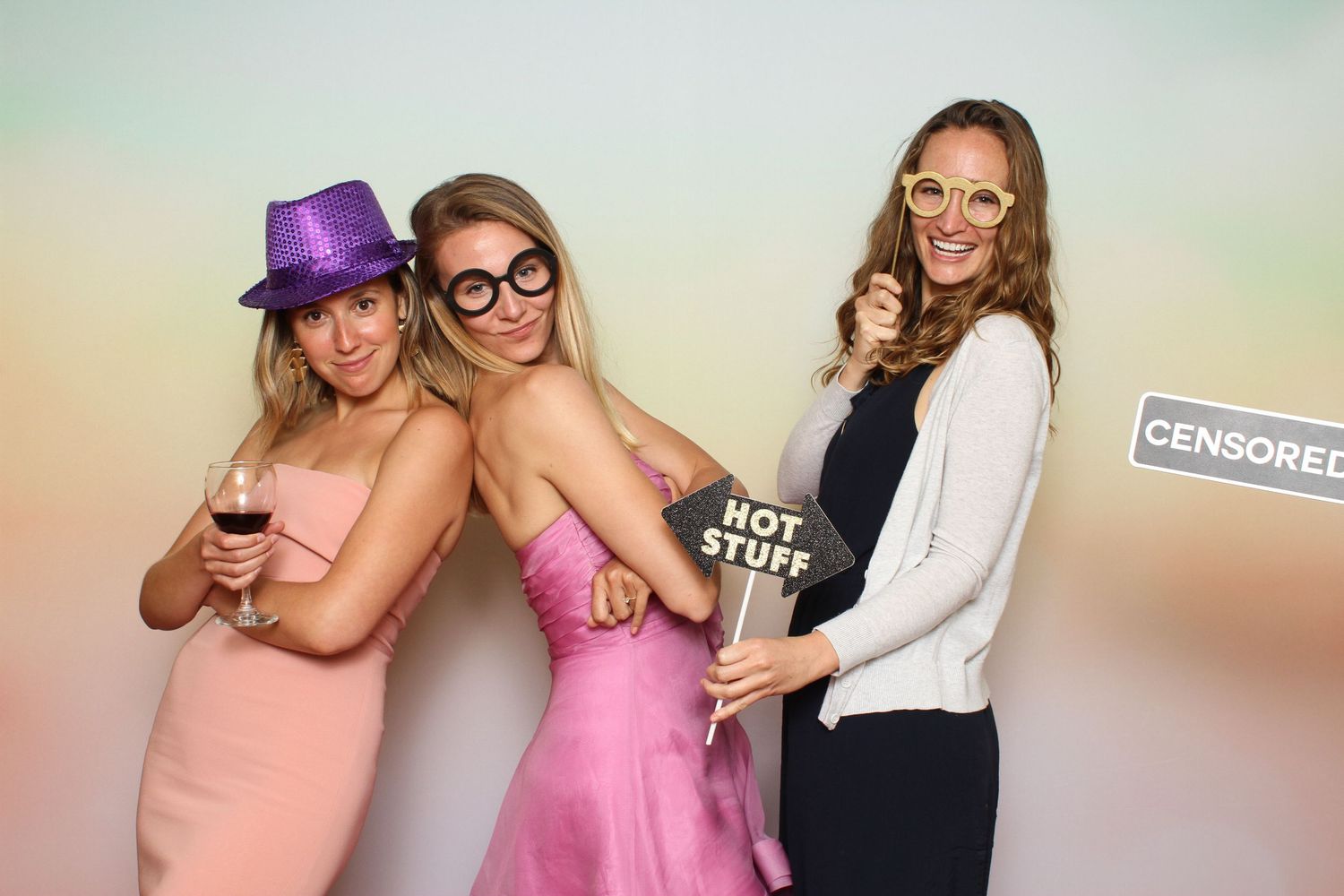 Three women posing playfully at a photo booth with fun props including hats, glasses, and a Hot Stuff sign. Peacock Gap Golf Club