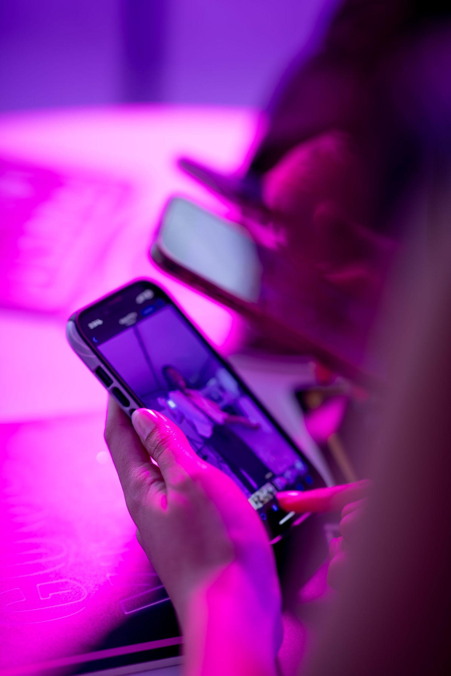 Person holding smartphone with camera app open in neon pink and purple lit environment.
