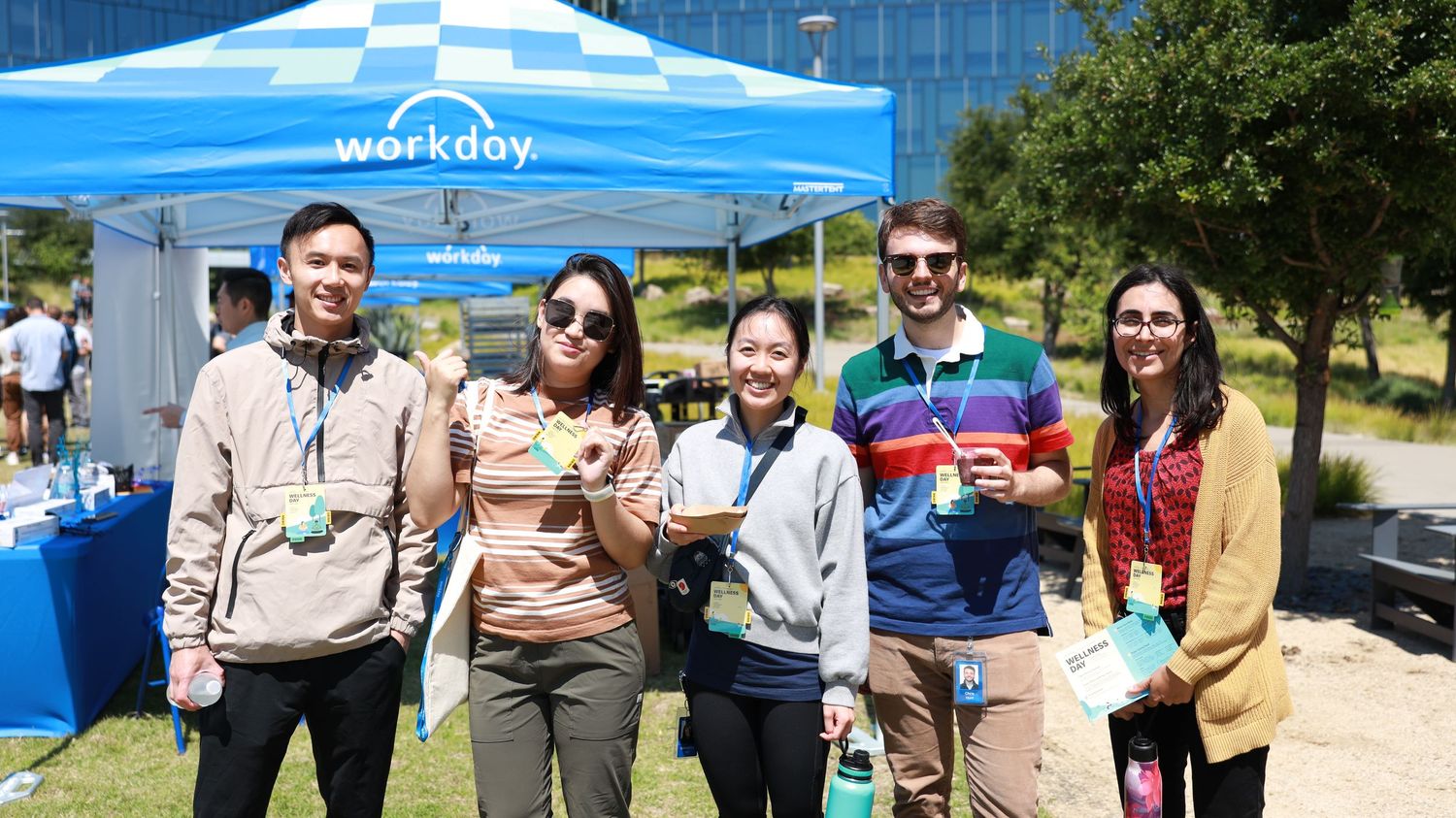 Five professionals smile together at a Workday outdoor corporate event on a sunny day.