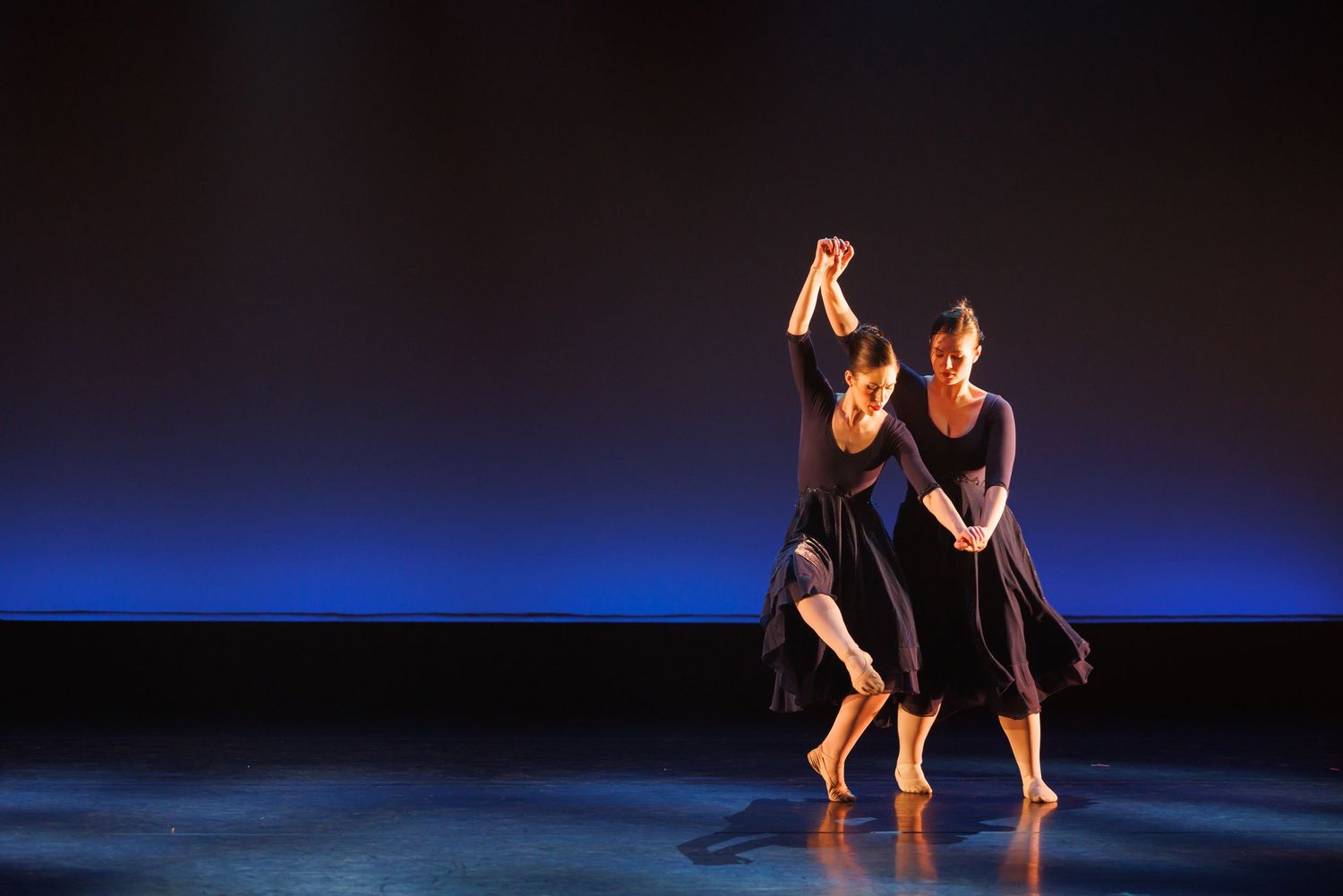 Two female dancers perform a contemporary duet on a dimly lit stage with blue lighting. Las Positas College
