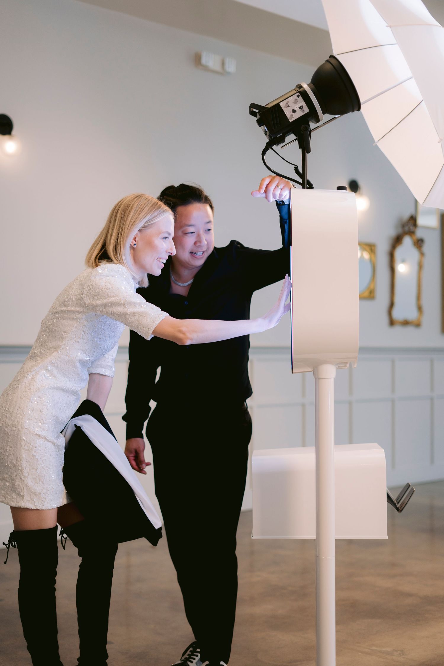 Lune photo booth. Two people examining a photo booth setup with studio lighting in an elegant white event venue.
