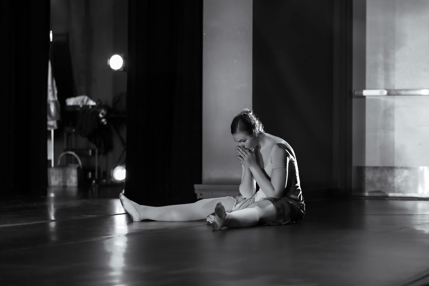 Black and white photo of a dancer sitting on studio floor, resting with legs extended in a contemplative pose. Las Positas College