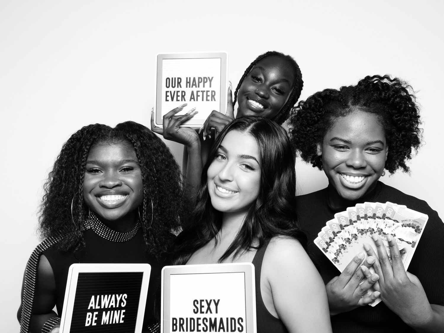 Four joyful bridesmaids posing with fun signs including Sexy Bridesmaids and Always Be Mine in black and white photo.