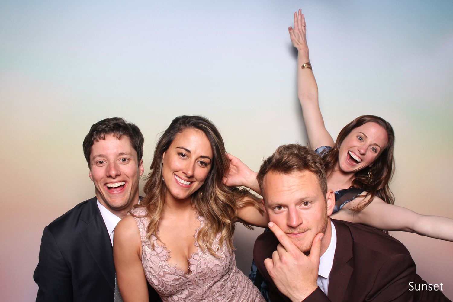 Group of four friends laughing and posing together in front of a sunset photo booth backdrop.