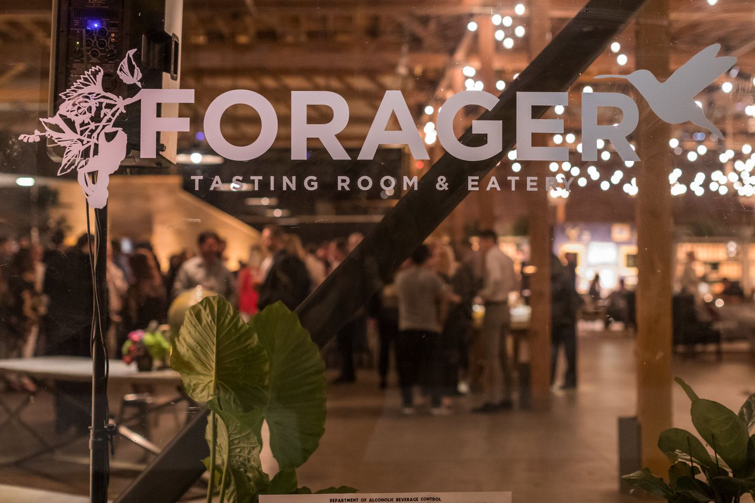 Forager Tasting Room & Eatery entrance sign with warm ambient lighting and guests mingling inside.