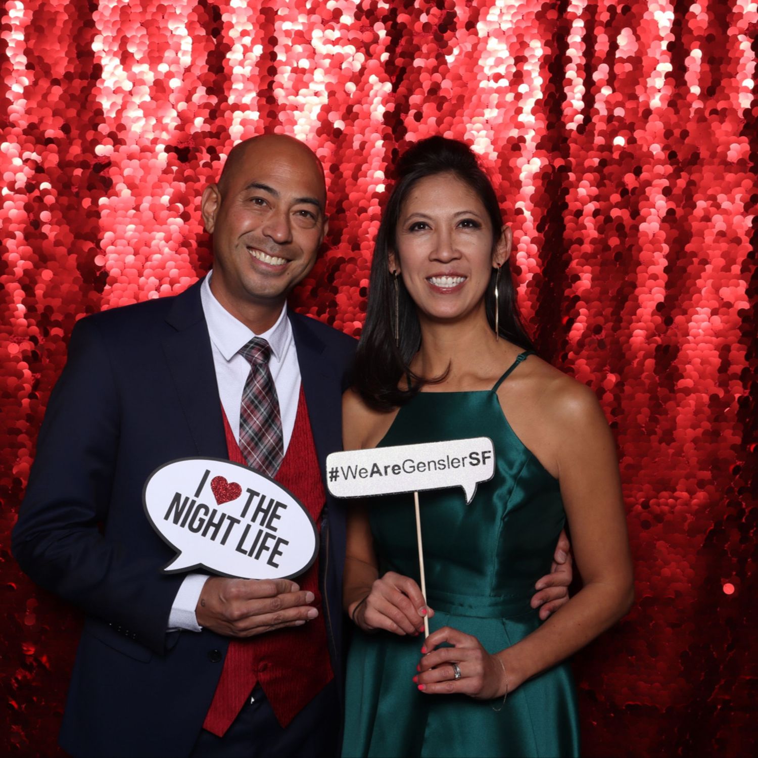 Two people posing at a Gensler SF event photo booth with red sequin backdrop holding fun signs at the Gensler San Francisco party.