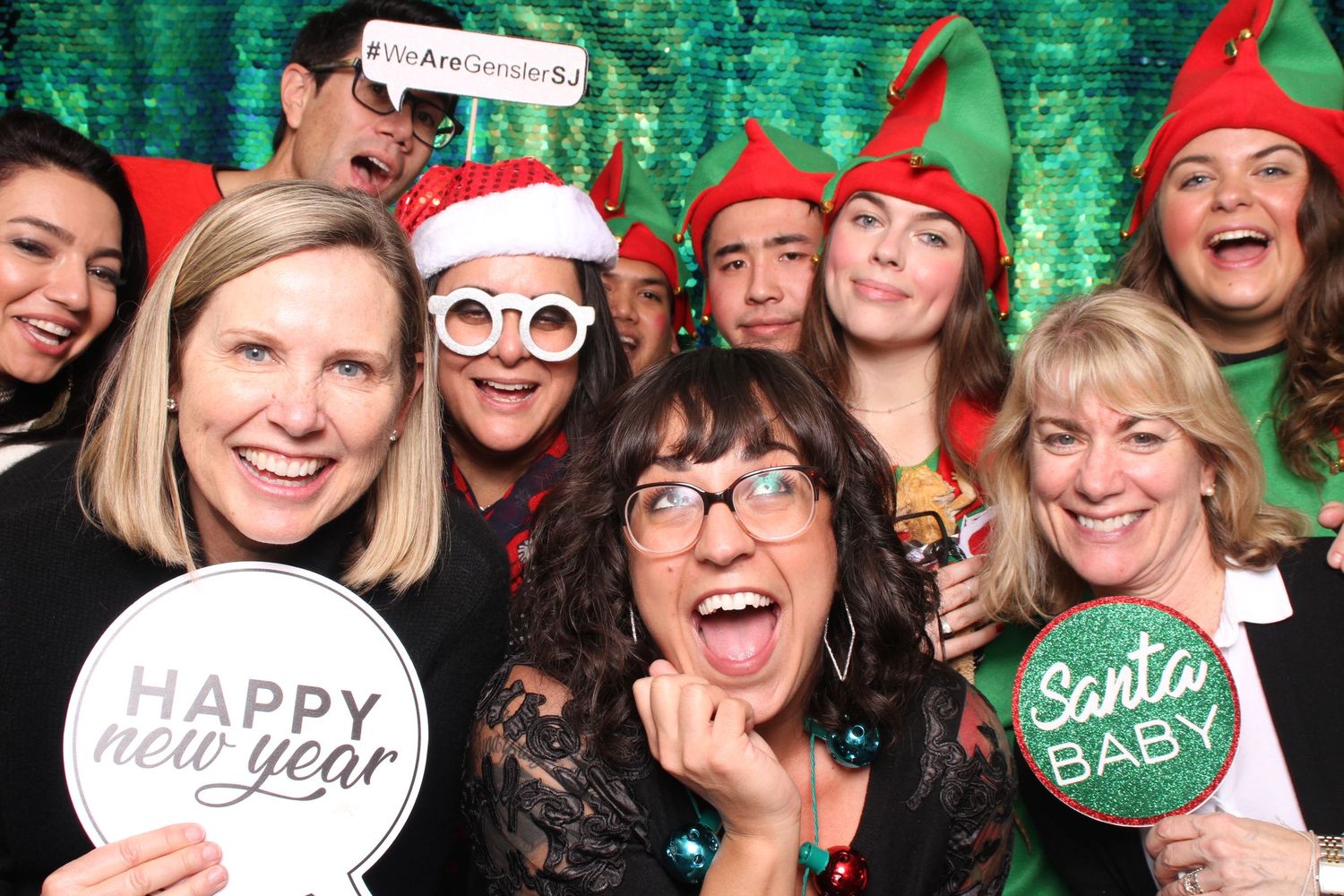 Group of coworkers celebrating at a Christmas holiday party photo booth with festive props and elf hats.