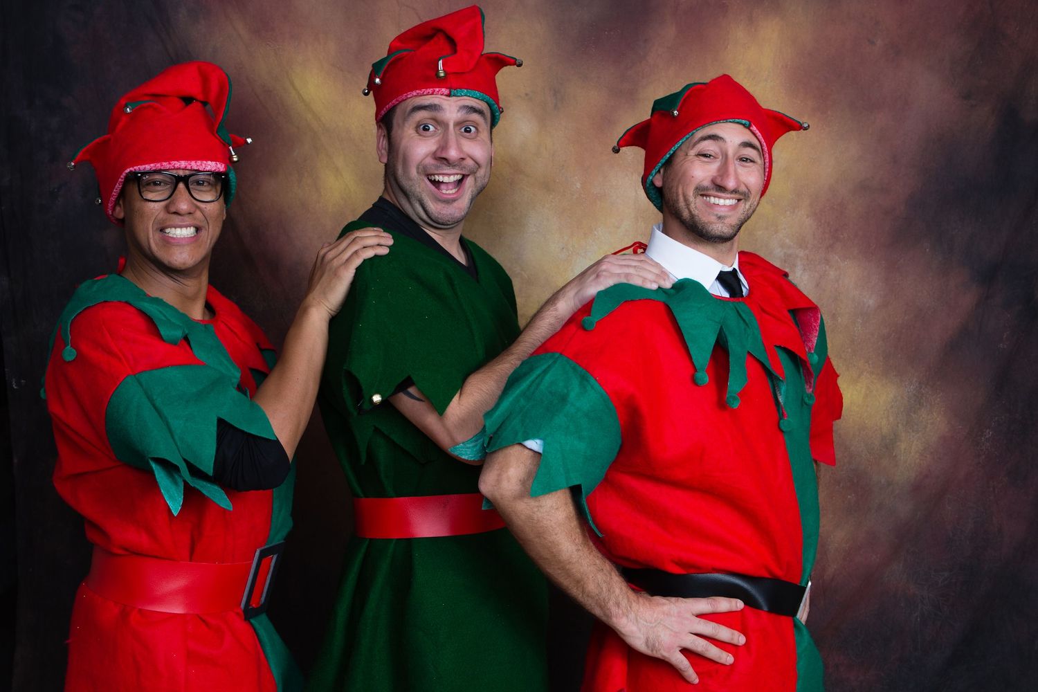 Three adults in red and green Christmas elf costumes pose playfully for a festive holiday photo. Gensler Holiday Party