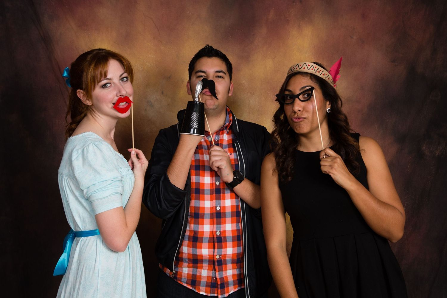Gensler Holiday Party Three friends pose with fun photo booth props including fake lips, mustache, and glasses against a studio backdrop.