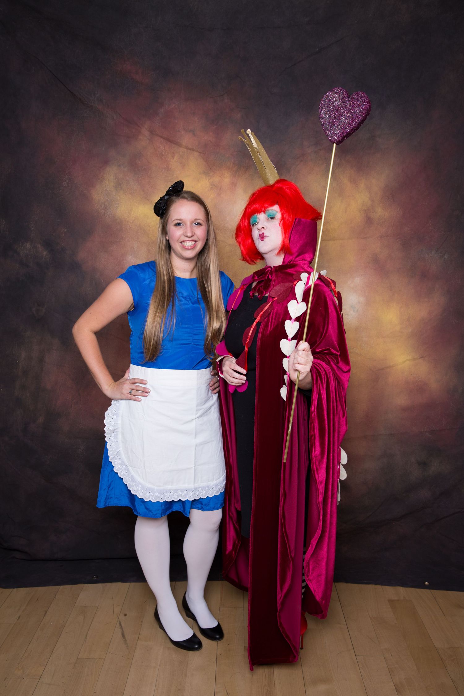 Two women in Alice in Wonderland costumes pose together, one as Alice and one as the Queen of Hearts. Gensler Holiday Party