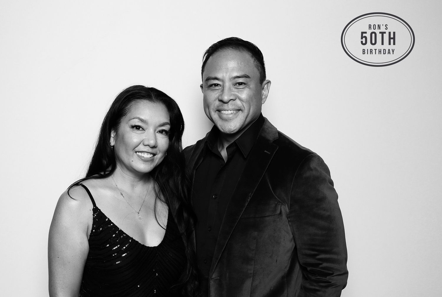 A smiling couple poses together at a 50th birthday celebration in a black and white photo booth portrait. Industrious, Walnut Creek.