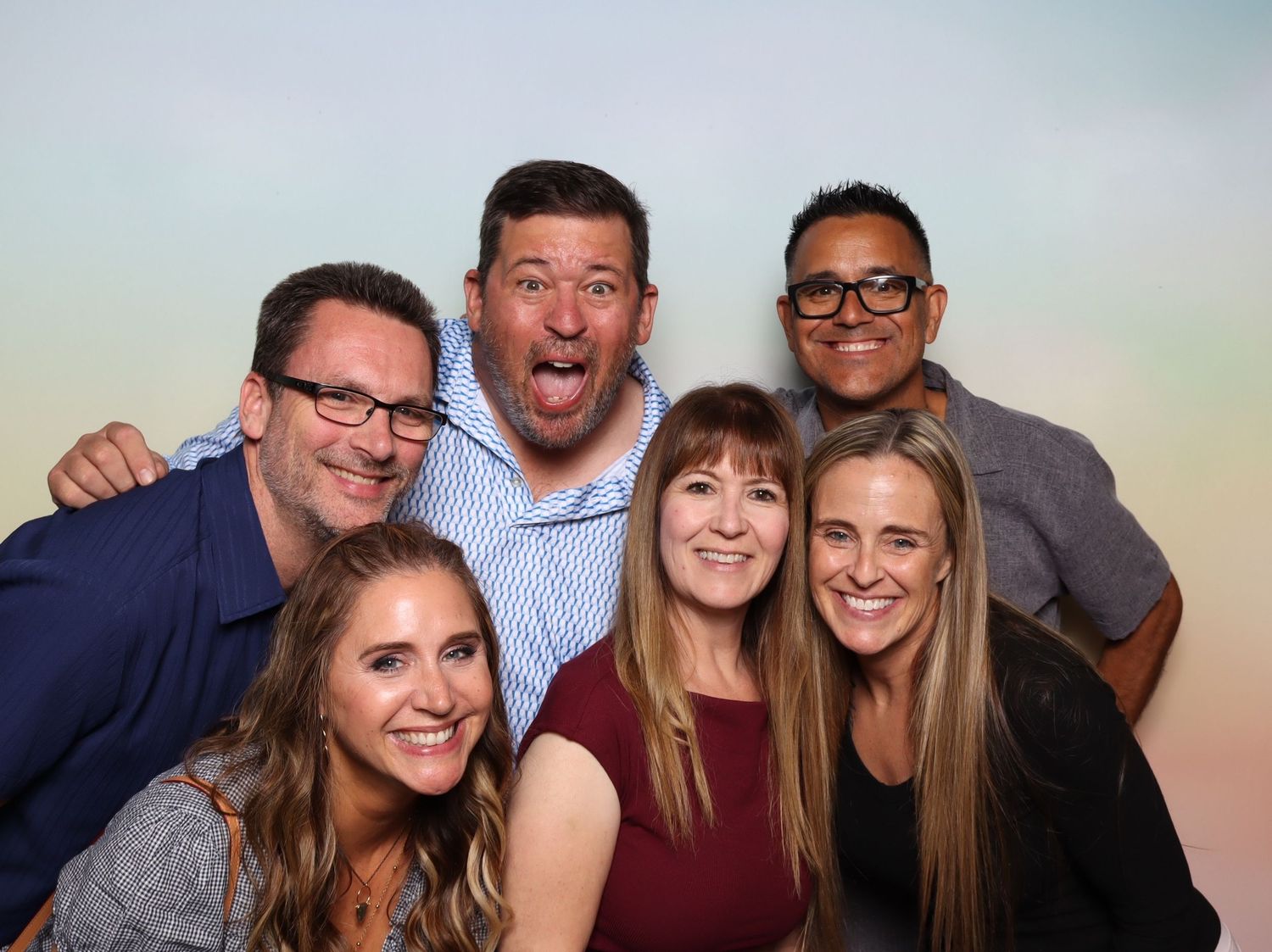 Six friends smile and pose together in a fun group photo booth picture with a bright pastel background at the Shine in Pleasanton.