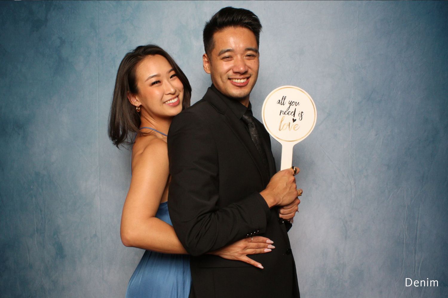 Couple posing together at formal event, woman in blue dress and man in black suit holding a round sign.