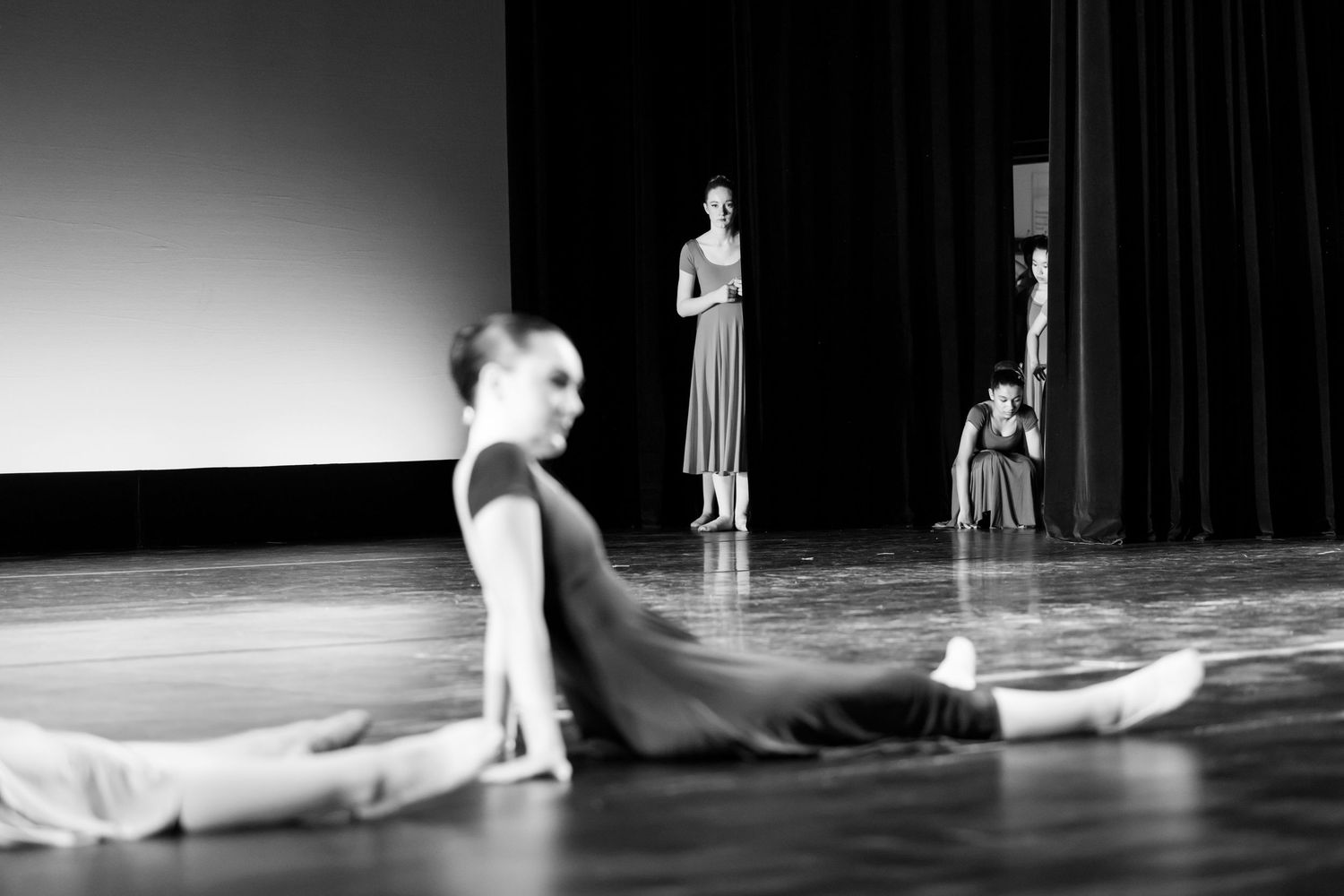 Black and white photo of ballet dancers performing on stage, with one dancer stretching in the foreground. Las Positas College