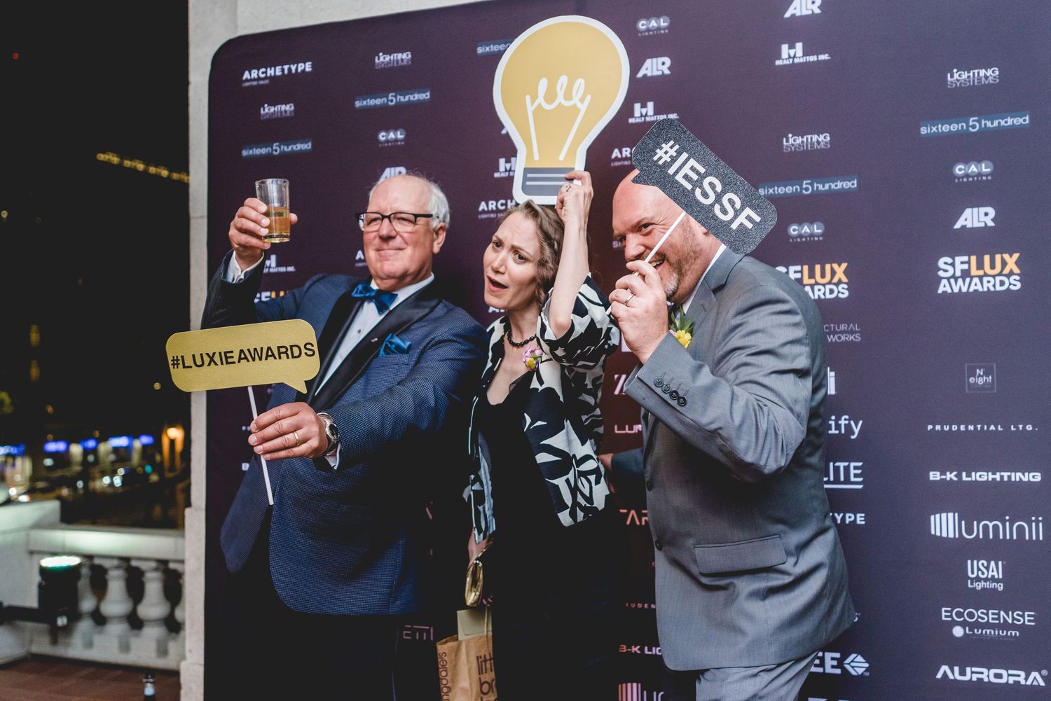 Three people posing playfully with FLUX IE Awards sign at an indoor awards ceremony event.