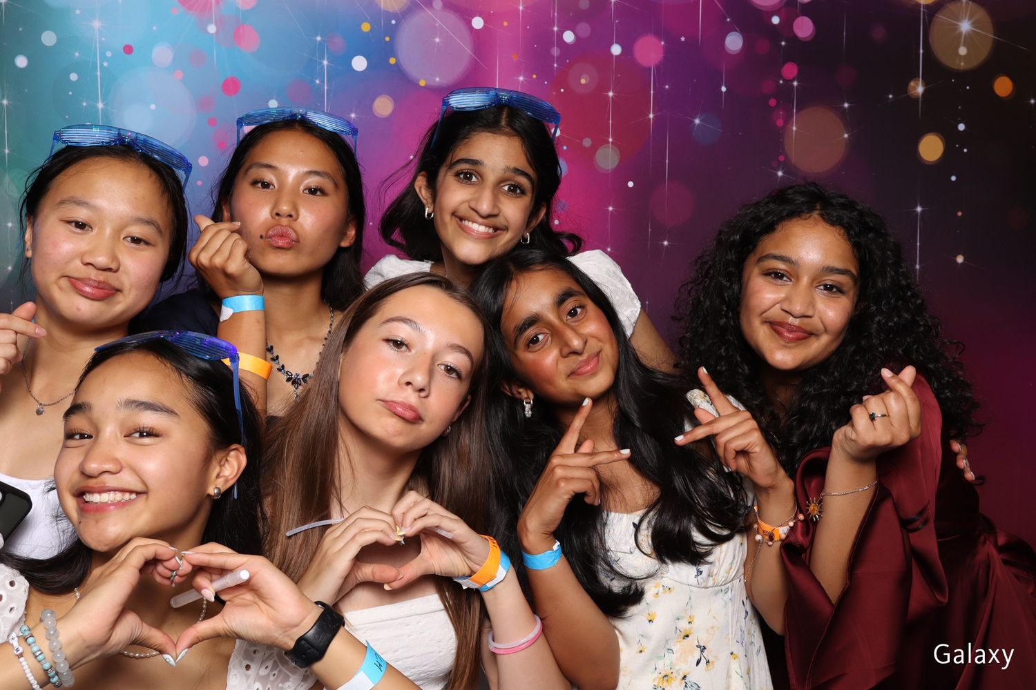 Group of eight young girls smiling and making fun poses in front of a Galaxy photo booth backdrop.