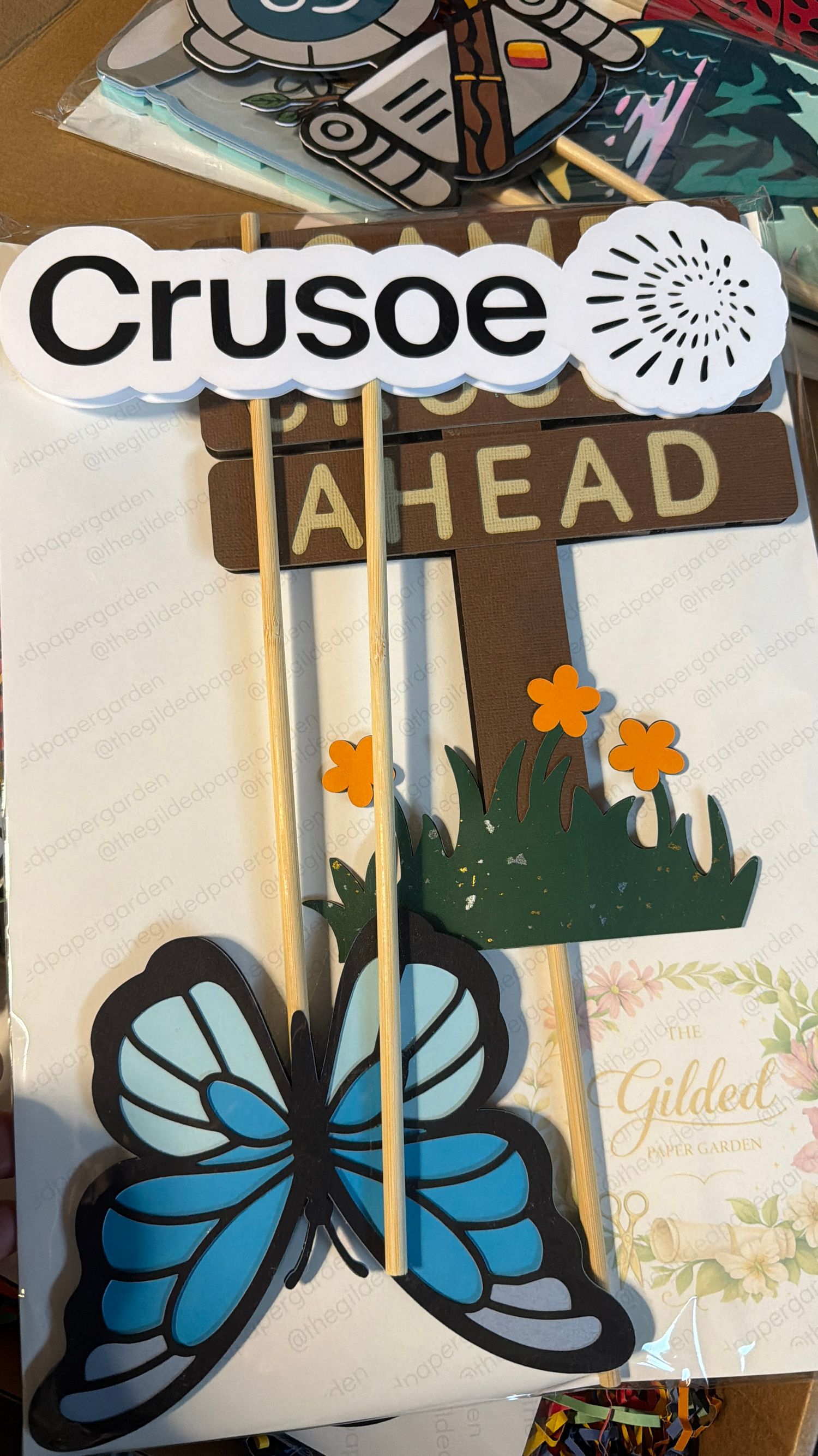 Crusoe themed custom props with butterfly, flowers, and adventure sign on wooden sticks.