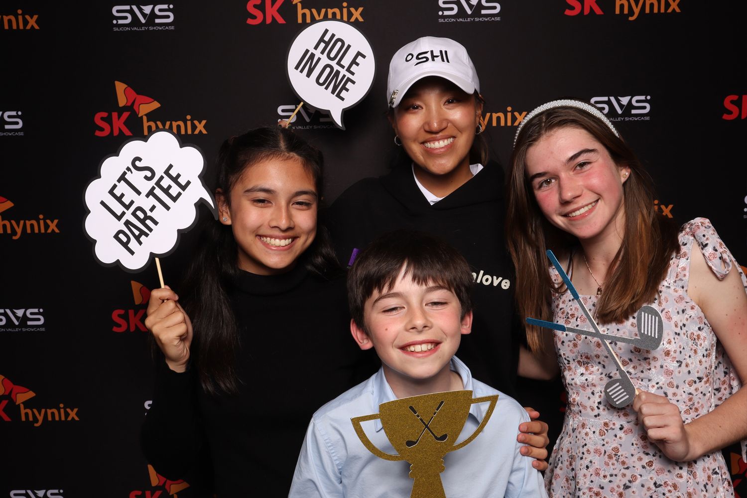 Four smiling people pose with golf props at an SK Hynix branded photo booth event.