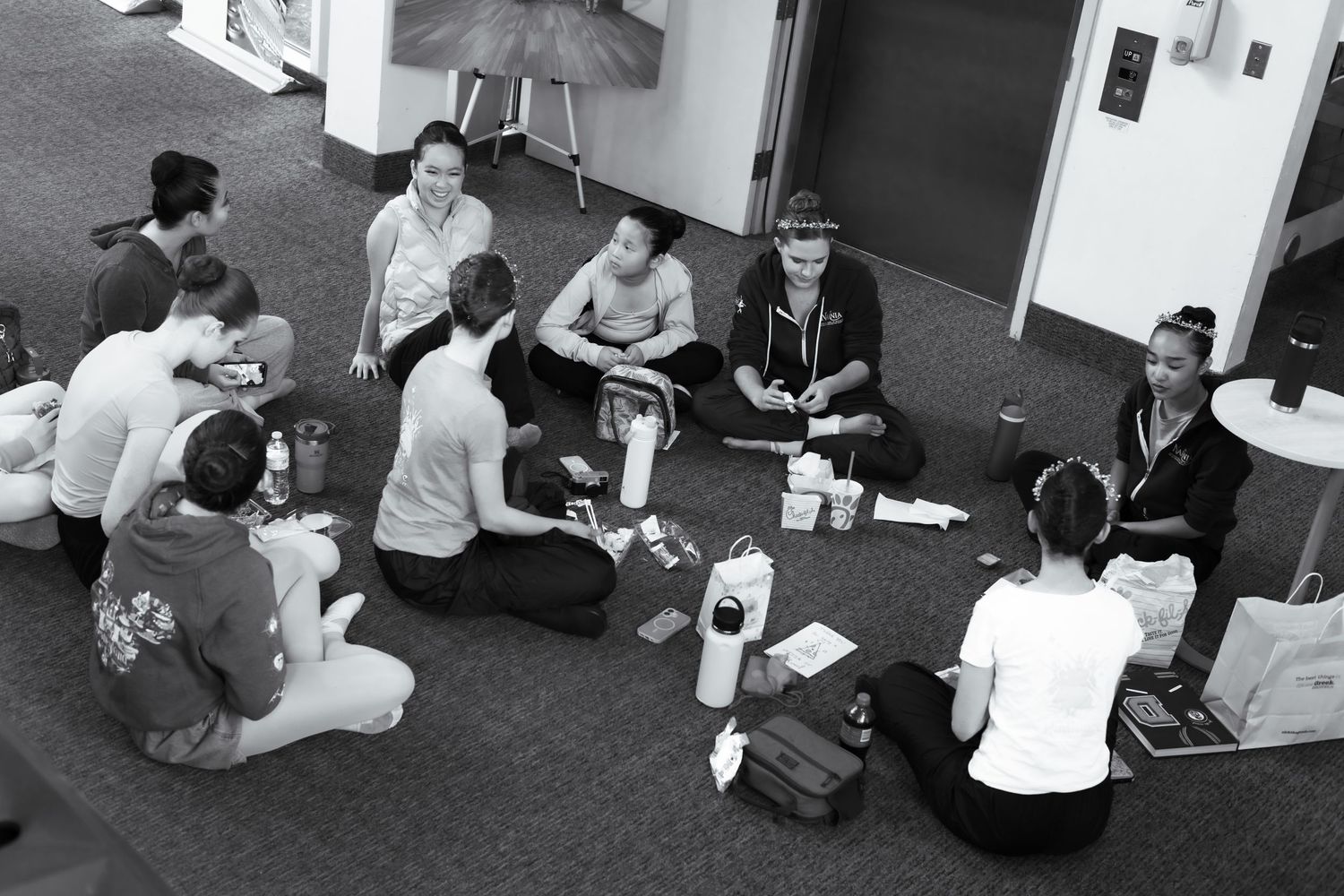 Group of people sitting in a circle on the floor playing a card game in a modern building interior. Las Positas College