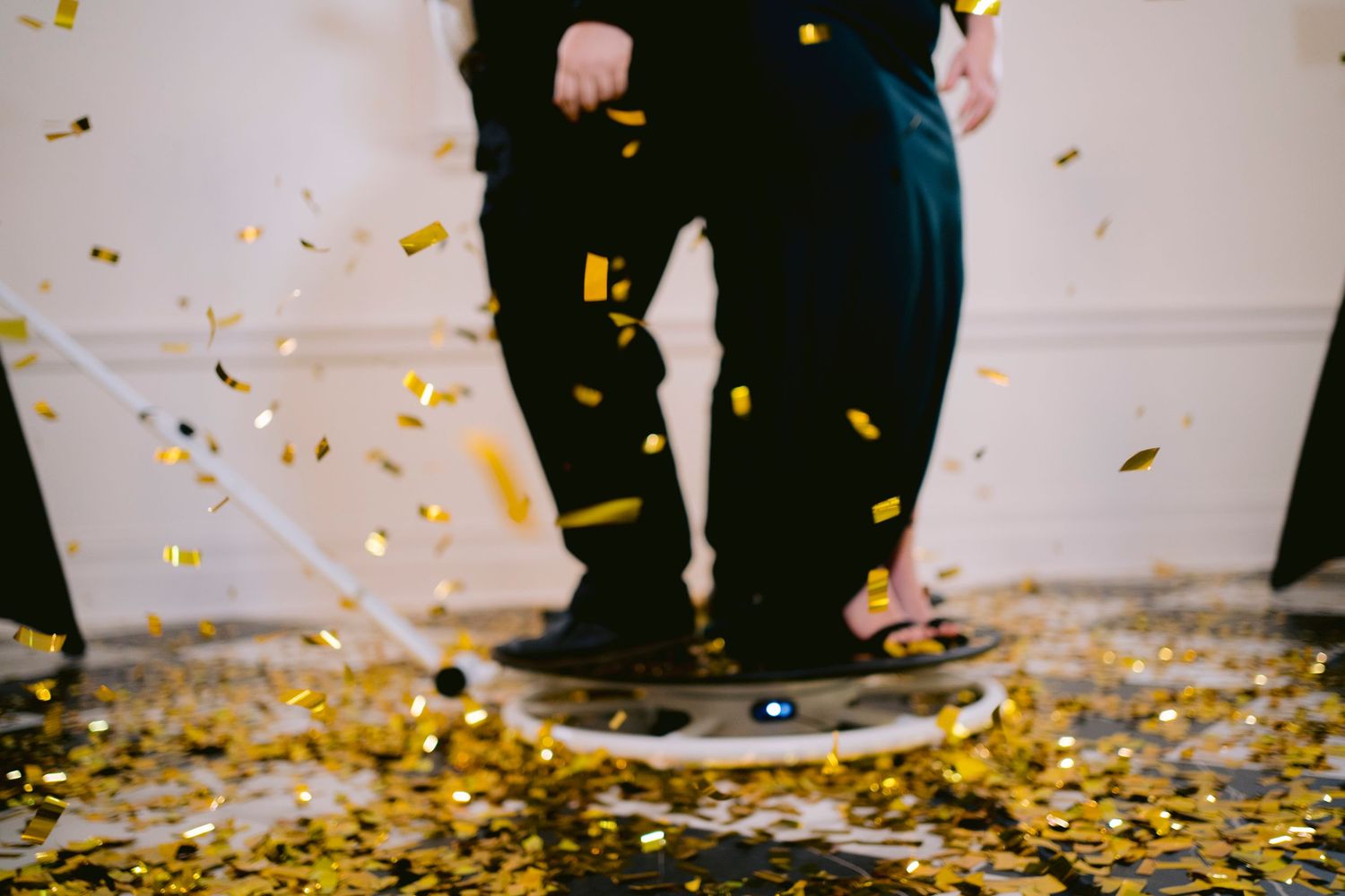 Two people standing on a rotating platform surrounded by golden confetti falling at a festive celebration event.