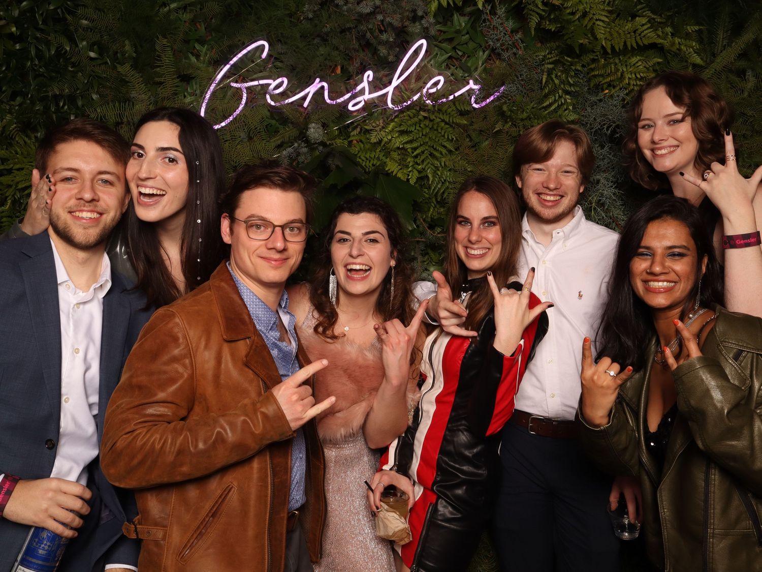 Group of young professionals smiling at a Gensler holiday party with green floral backdrop at the Fillmore Center in San Francisco