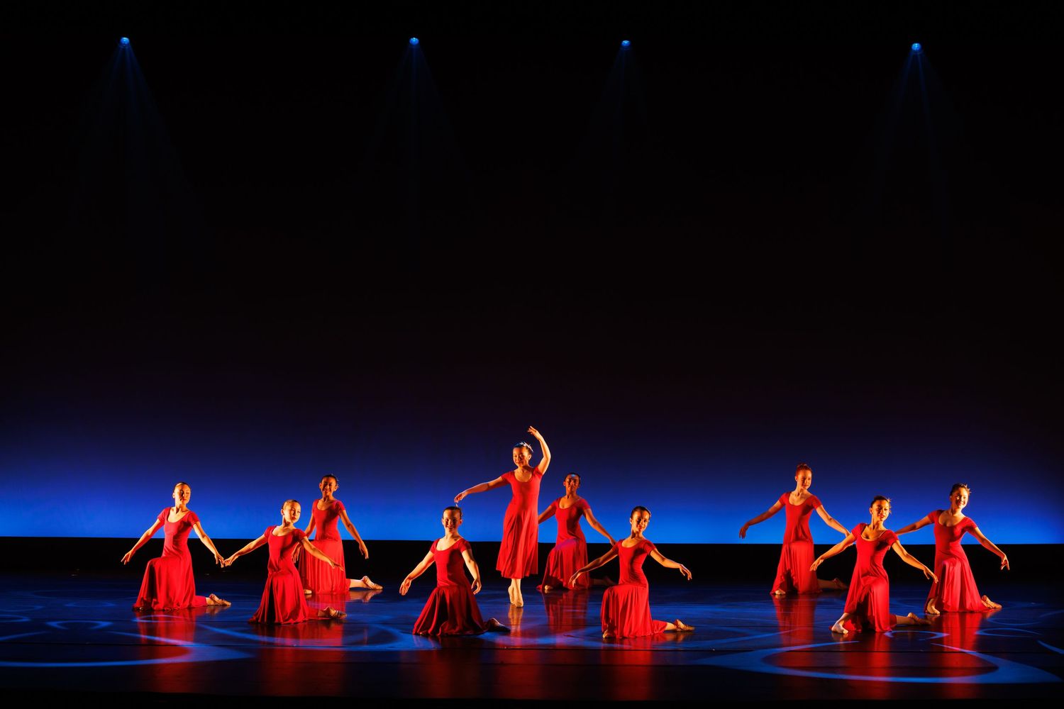 Dancers in red dresses perform on a blue-lit stage in a stunning group dance performance. Las Positas
