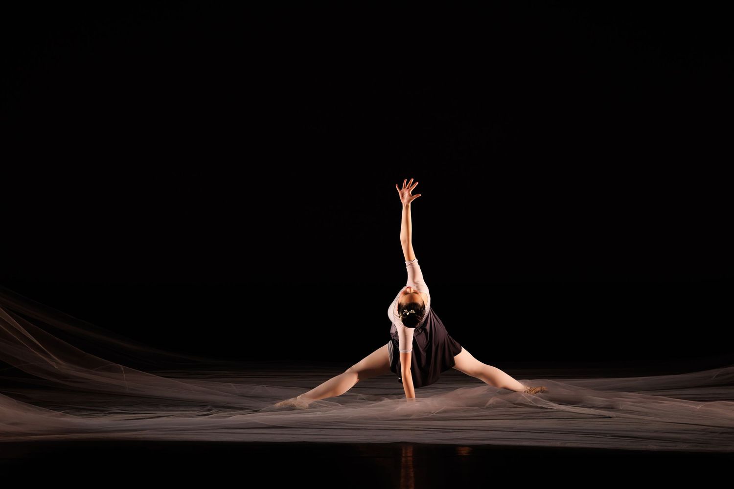 A ballet dancer performs an elegant split on stage, one arm raised Las Positas College in Livermore.