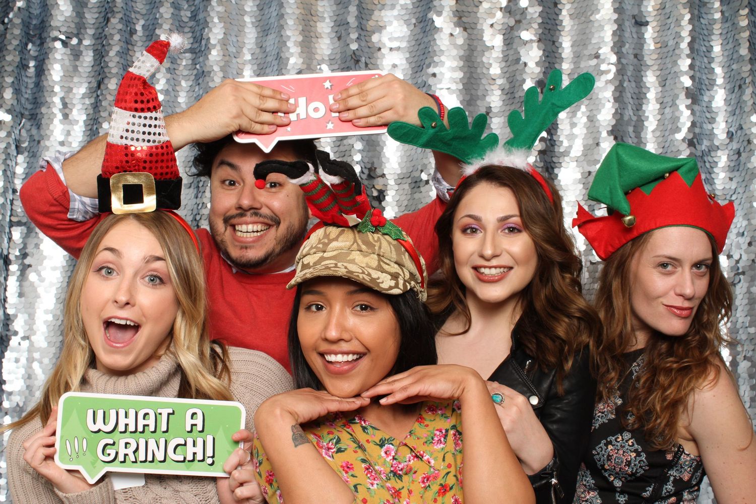 Five friends pose in Christmas hats and antlers at a holiday photo booth with a 