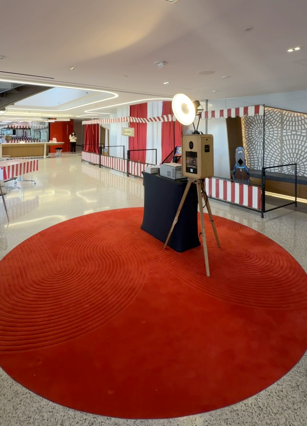 Modern lobby with red circular rug, vintage photo booth on tripod, and red-white striped carnival-themed decor at an event in San Francisco.