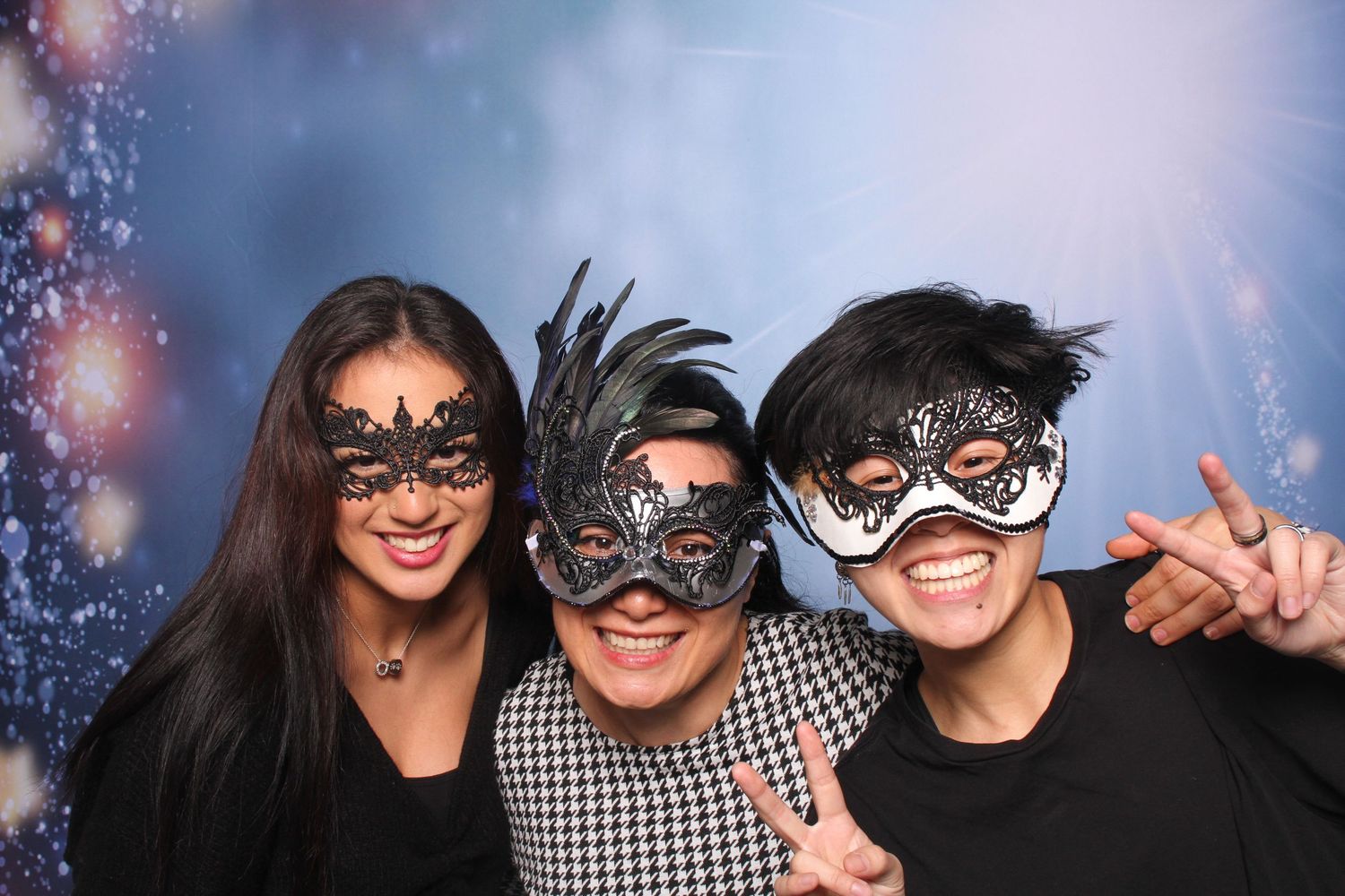 Three friends wearing elegant black masquerade masks smile and pose together at a festive masquerade party event. at Festivus at KBM Hogue's