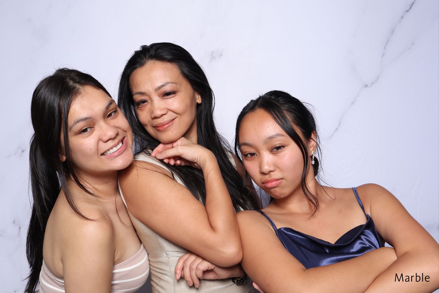 Three young women posing together in front of a marble photo booth backdrop.