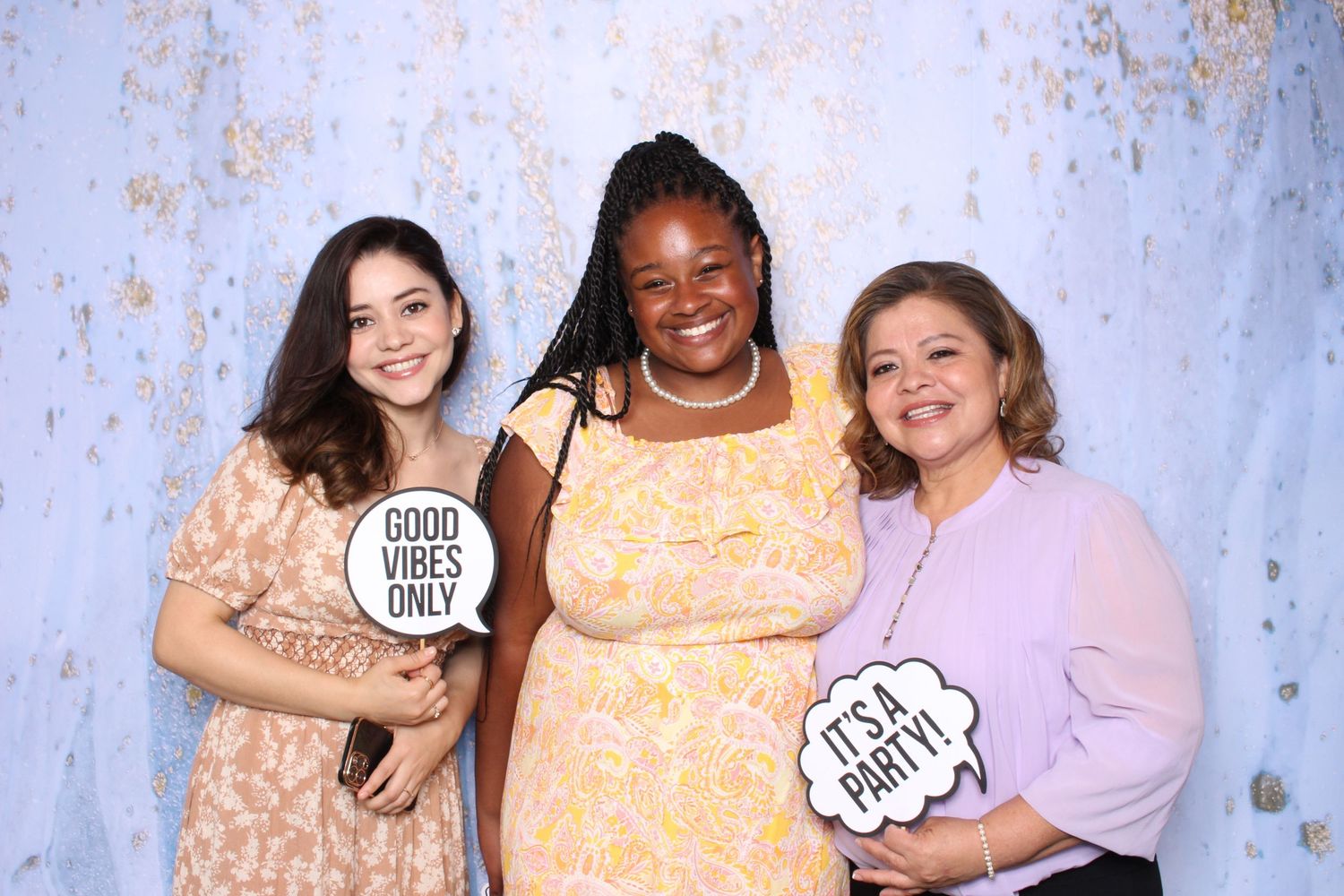 Three women smile at a party photo booth holding Good Vibes Only and Its a Party signs.