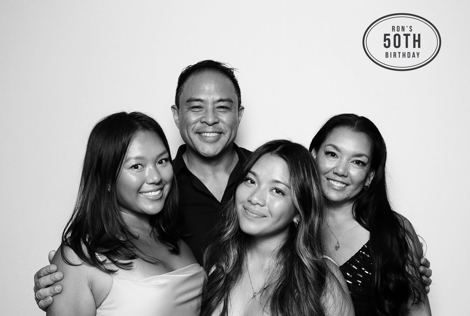 Black and white photo booth picture of four smiling people celebrating a 50th birthday party. Industrious, Walnut Creek.