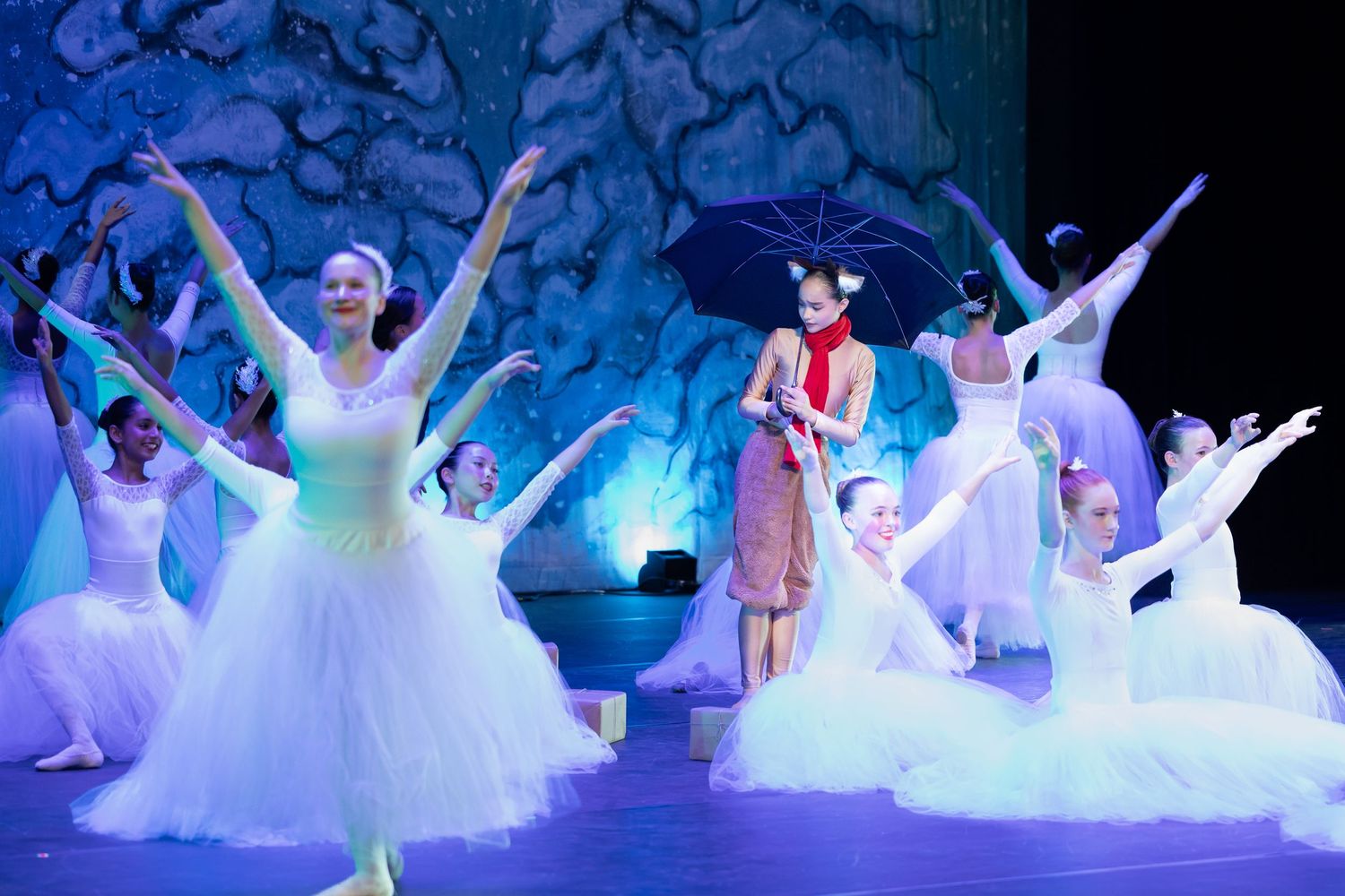 Young ballerinas in white tutus perform on stage during a Nutcracker ballet recital under blue stage lighting.