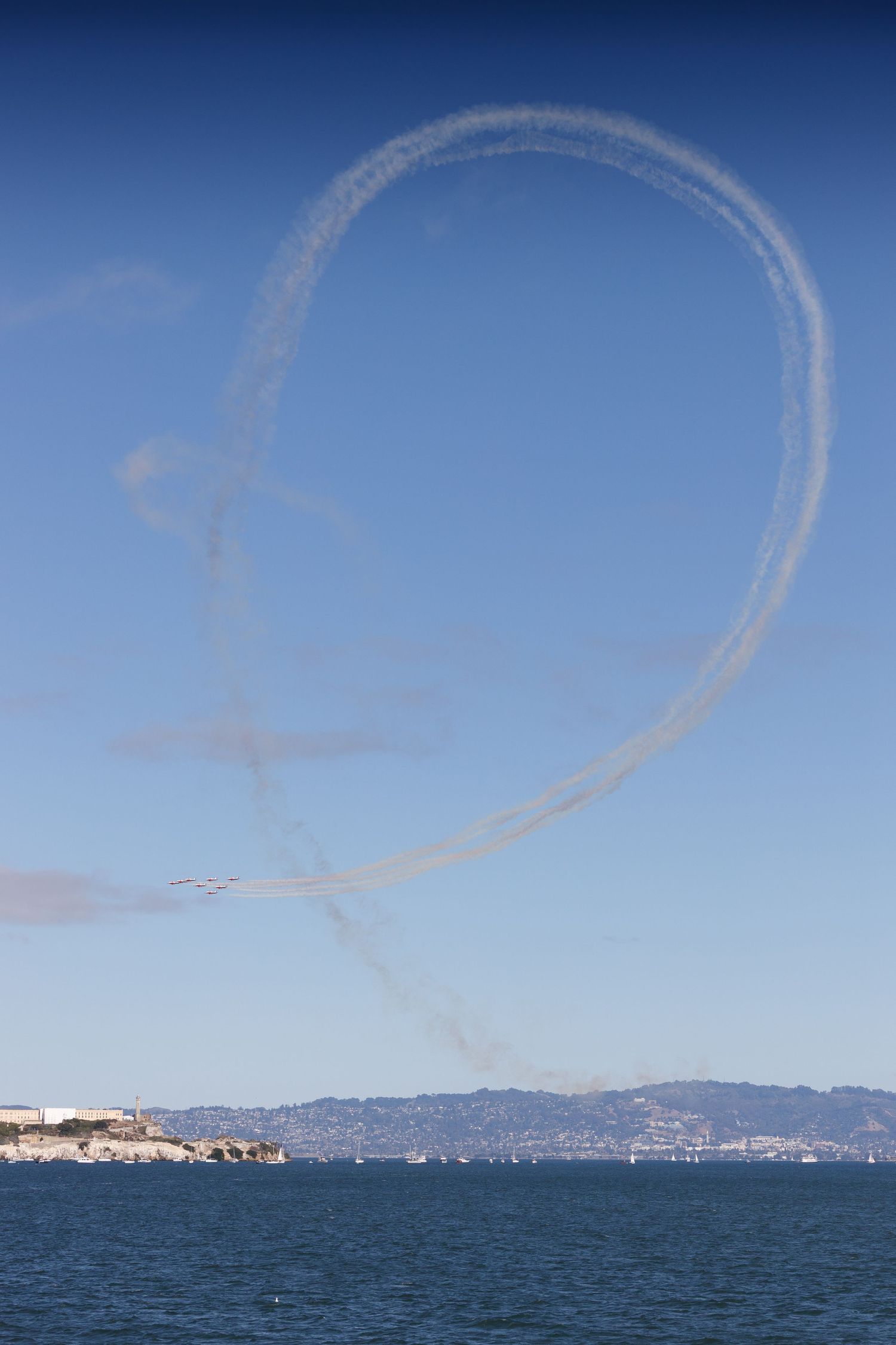 Aircraft performing loop maneuver with smoke trail over San Francisco Bay, Alcatraz Island visible below.
