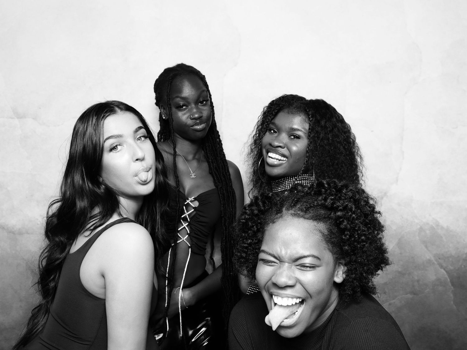 Four young women posing playfully in a black and white photo booth picture, making fun expressions.