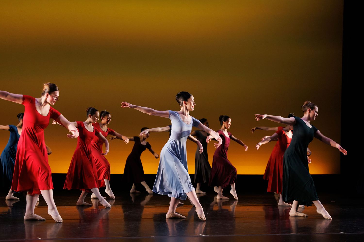 Dancers in red and blue gowns perform a contemporary ballet on a warmly lit stage. Las Positas