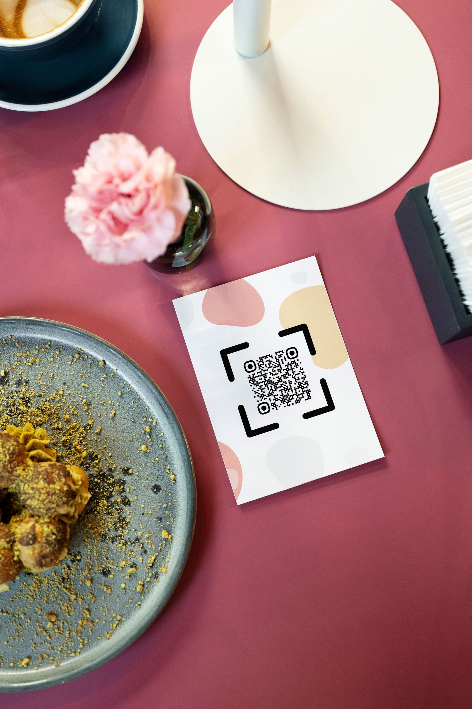 A Linktree Snapbox Collective QR code menu card on a pink restaurant table with a ceramic plate of food, pink flower, and coffee cup.