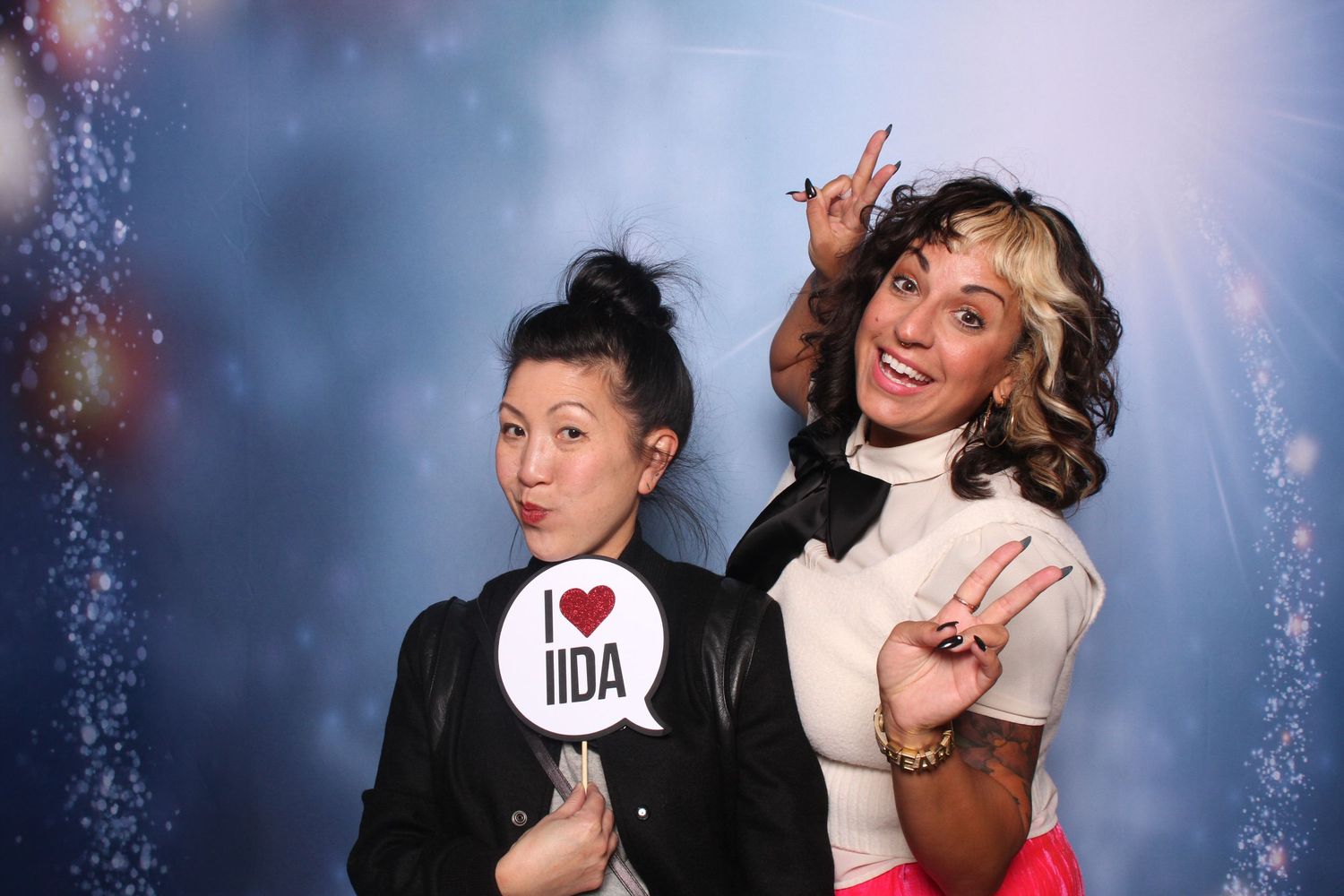 Two women pose playfully at an IIDA event photo booth at Festivus at KBM Hogue's office in San Jose