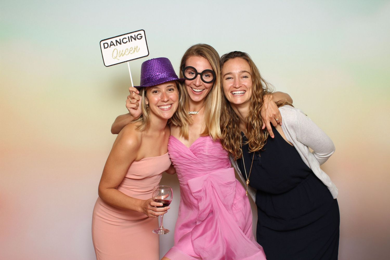 Three women posing at a photo booth, one holding a Dancing Queen sign and wearing novelty glasses at a party. Peacock Gap Golf Club
