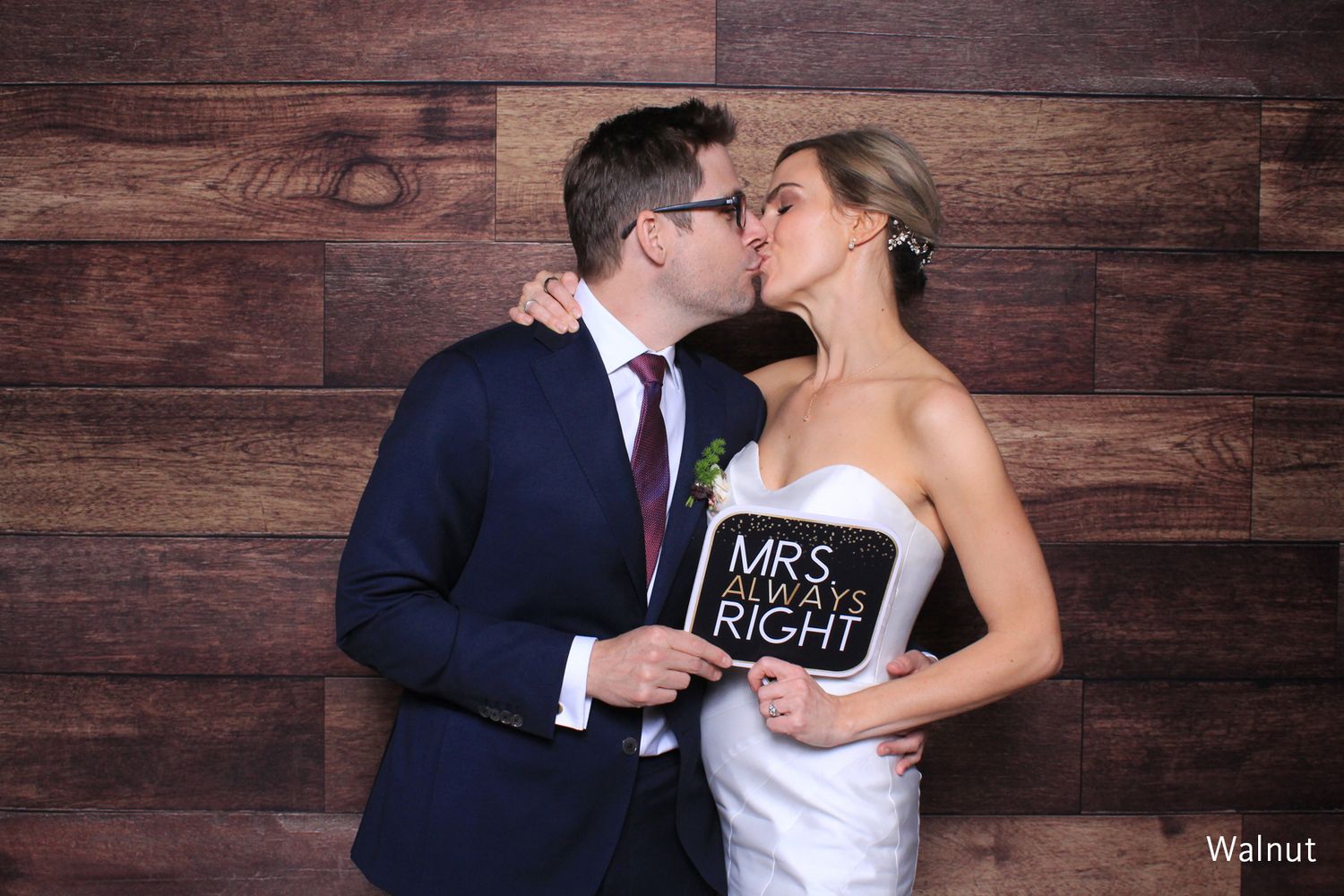 Newlyweds kissing in photo booth holding Mrs Always Right sign against wood backdrop.