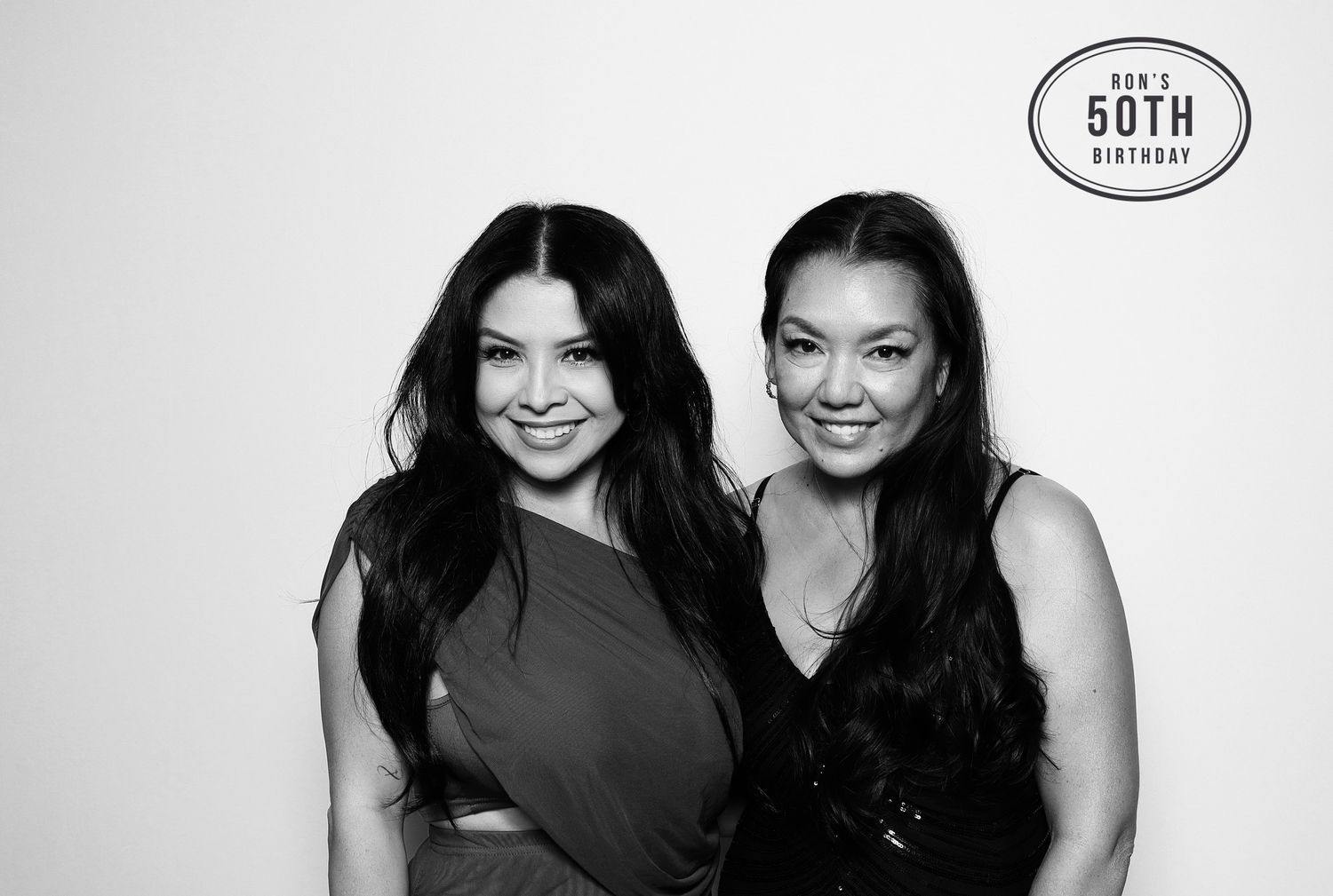 Two women smiling together at a 50th birthday celebration in a black and white photo booth portrait. Industrious, Walnut Creek.