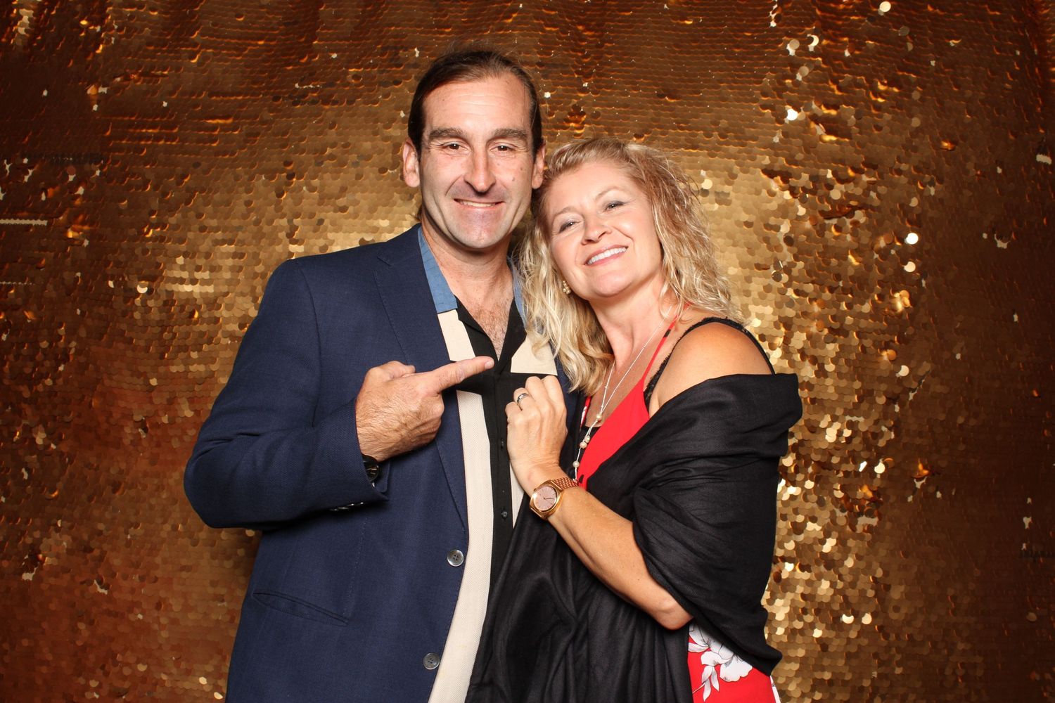 Smiling couple posing together at elegant event with gold glitter backdrop.