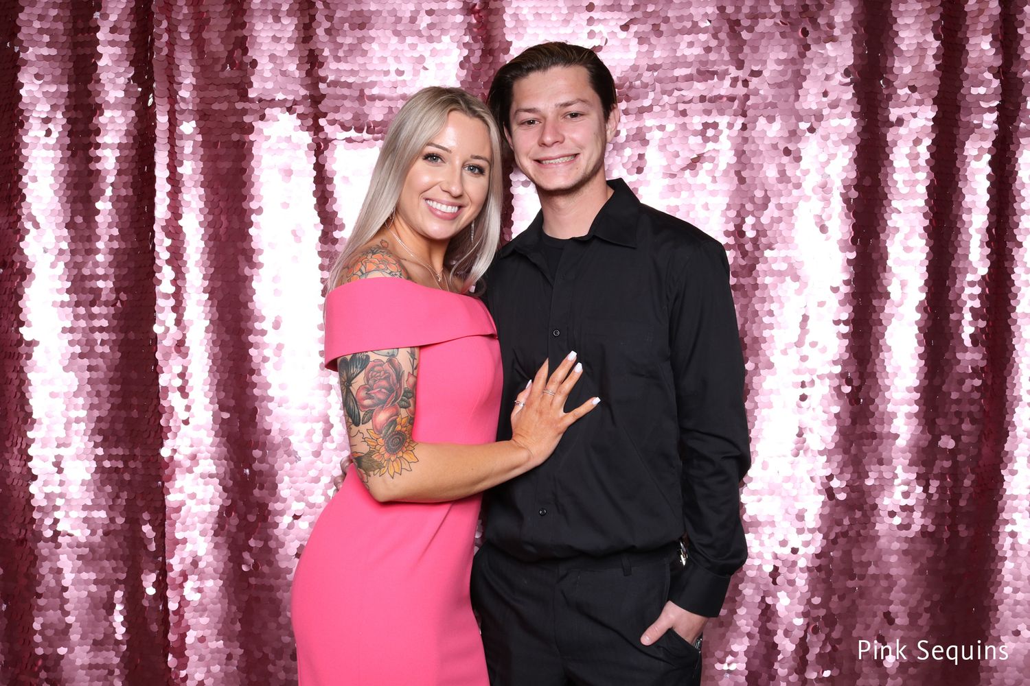 Couple posing together in front of pink sequin photo booth backdrop.