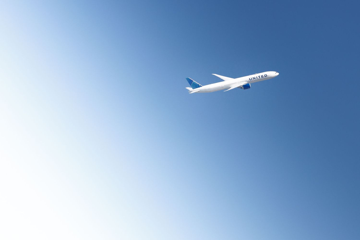 United Airlines airplane soaring through a clear blue sky, viewed from below on a sunny day.